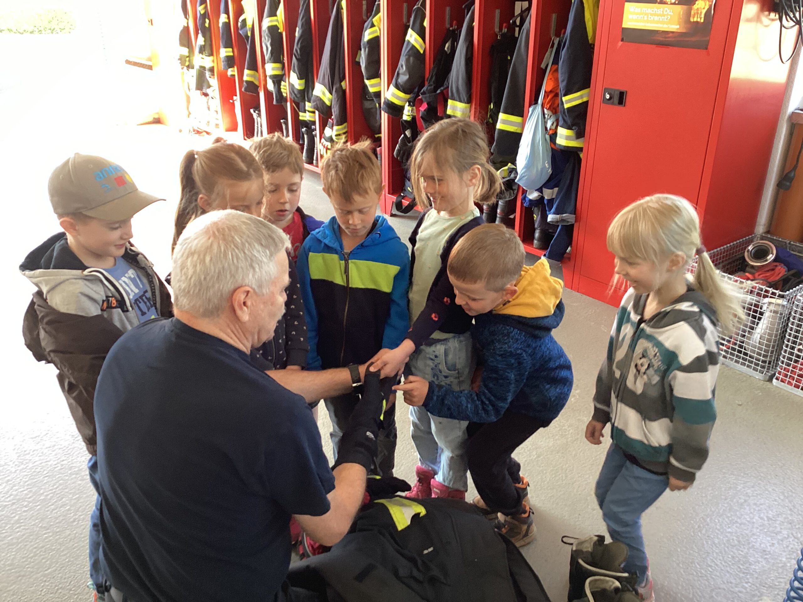 Feuerwehrmann legt zusammen mit den Kindern die Ausrüstung an